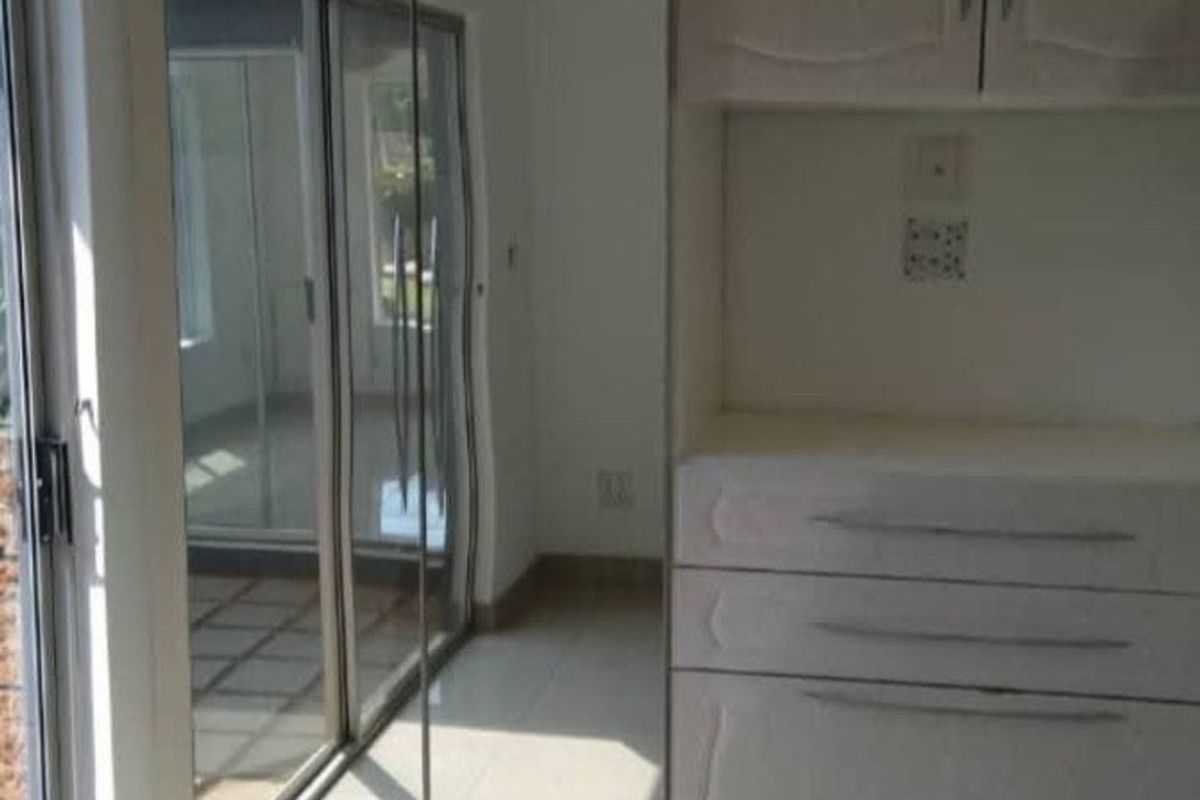 A bright, empty bedroom featuring tiled flooring, built-in cupboards with mirrored doors, and a sliding glass door providing access to the exterior.