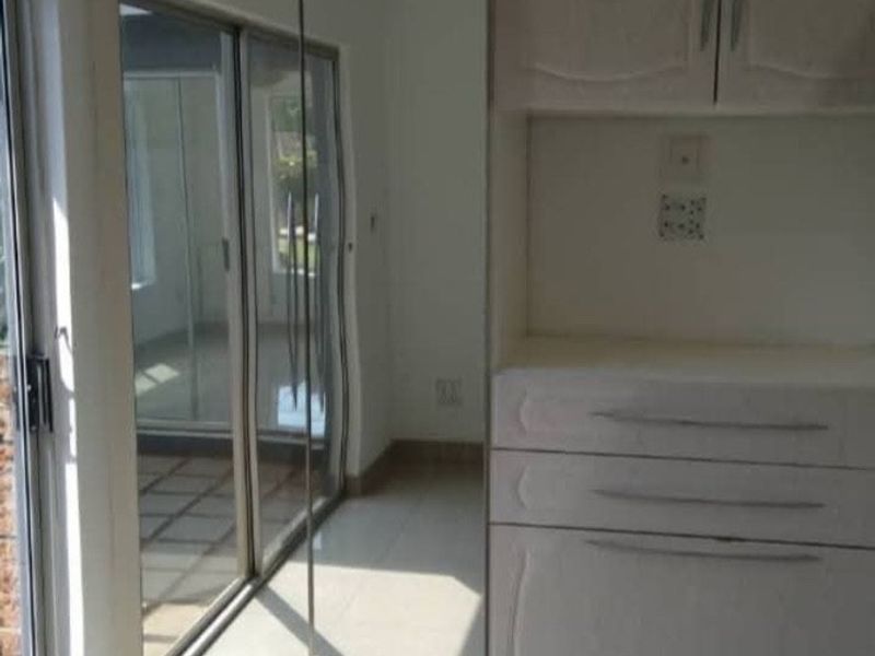A bright, empty bedroom featuring tiled flooring, built-in cupboards with mirrored doors, and a sliding glass door providing access to the exterior.
