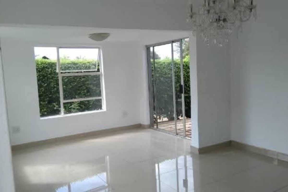 A bright, empty living area featuring polished tiled flooring, a crystal chandelier, and sliding glass doors leading to the garden.
