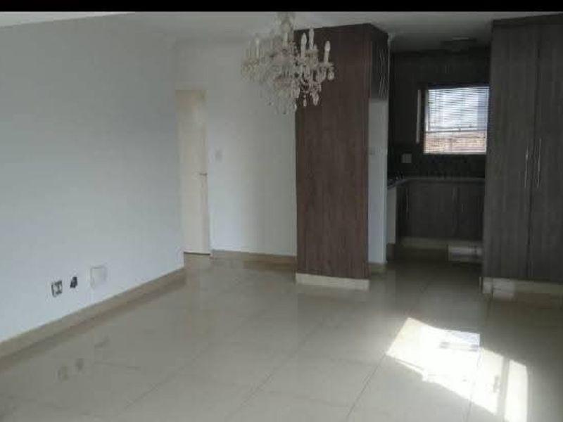 An open-plan living and kitchen area featuring tiled flooring, built-in cabinetry, and a central chandelier in a bright, vacant space.