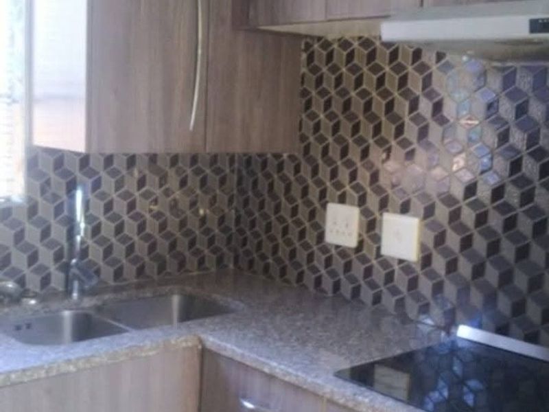 Compact kitchen featuring wood-look laminate cabinetry, stone-effect countertops, a geometric mosaic tile backsplash, and integrated stainless steel appliances.