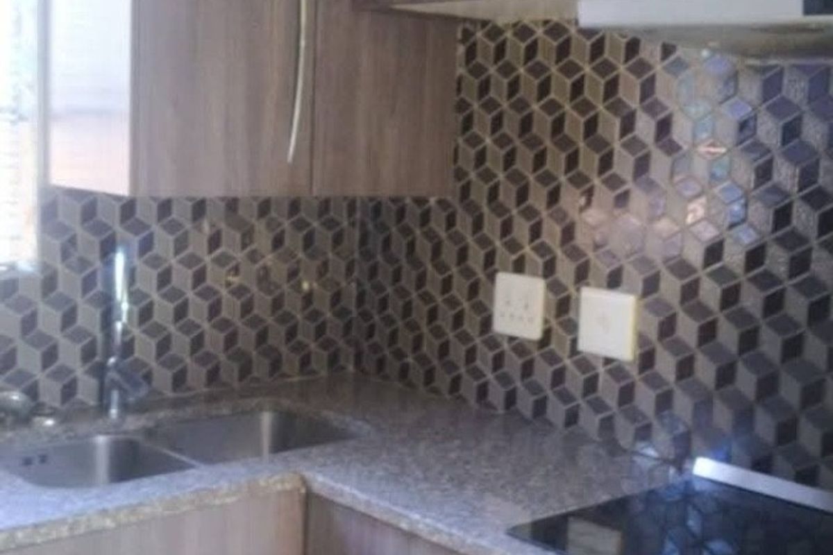 Compact kitchen featuring wood-look laminate cabinetry, stone-effect countertops, a geometric mosaic tile backsplash, and integrated stainless steel appliances.