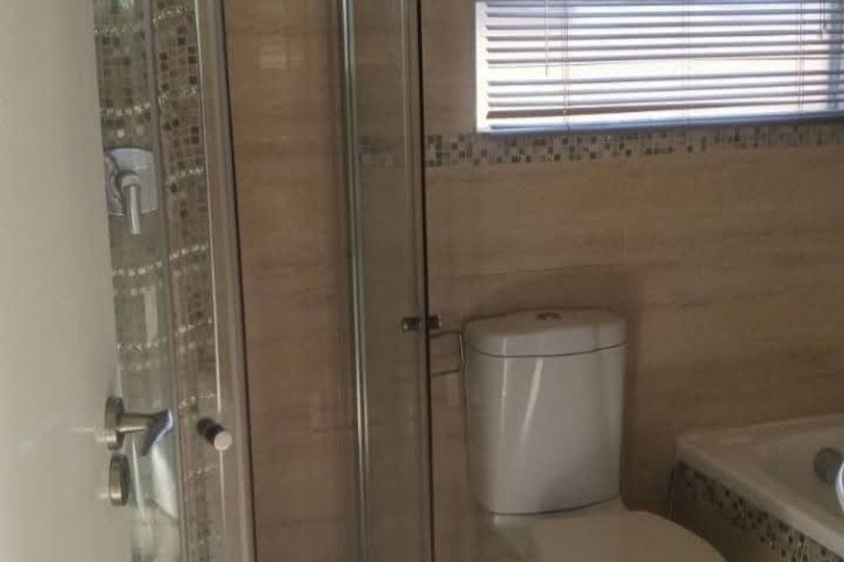 A functional bathroom featuring a curved glass shower enclosure, toilet, and tiled walls with a decorative mosaic border.
