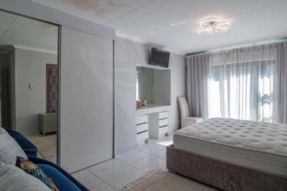 Spacious bedroom featuring built-in cupboards with mirrored doors, a built-in vanity, and tiled flooring. Note visible ceiling water staining requiring attention.