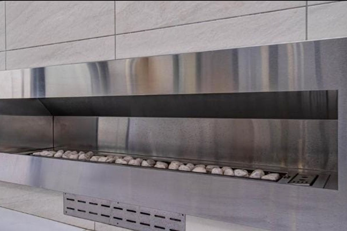 A modern, built-in stainless steel fireplace set into a tiled stone feature wall, providing a sleek and contemporary focal point.