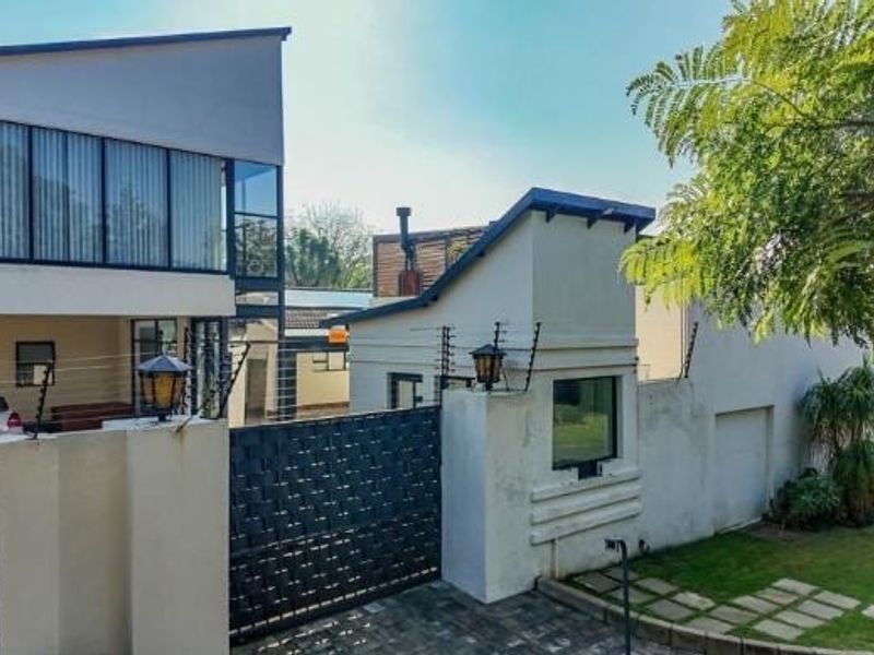 Front elevation of a modern multi-level house featuring a secure gated entrance, electric fencing, paved driveway, and a well-maintained front garden.
