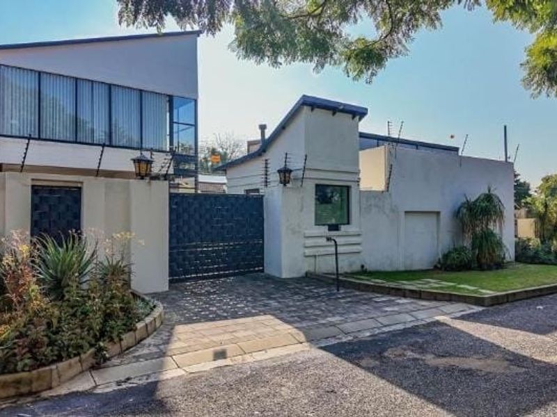 Front elevation of a modern house featuring a paved driveway, secure gated entrance, and perimeter boundary walls with integrated electric fencing.