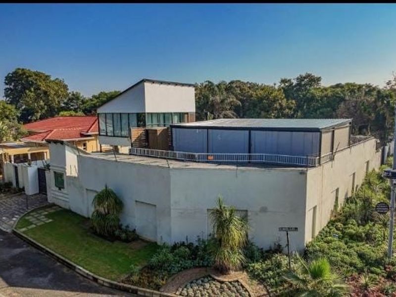 An elevated view of a modern residential property featuring a unique architectural design, perimeter security walls, and established garden landscaping.