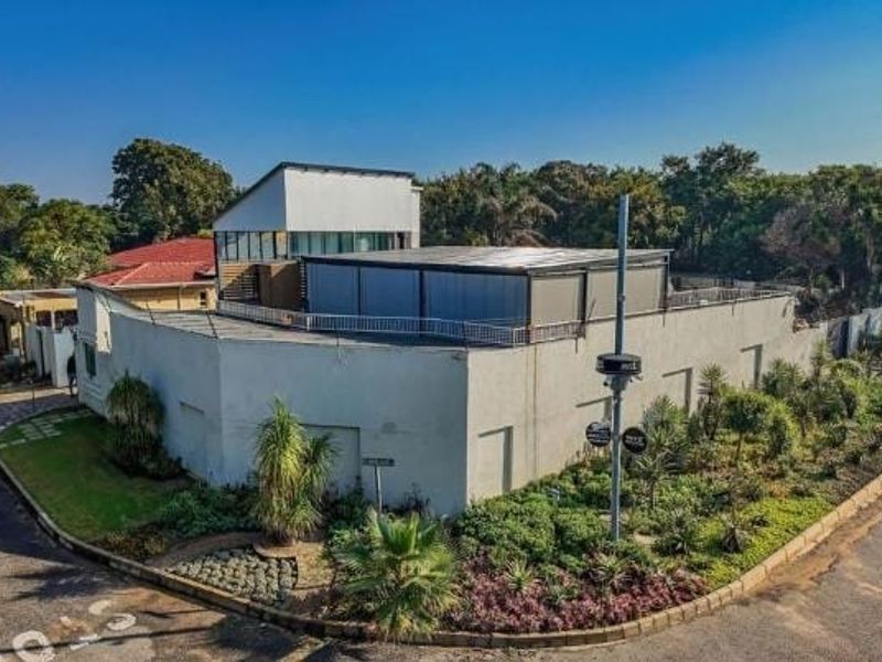 An elevated view of the property exterior, showcasing the modern building structure, security features, and landscaped garden area on a corner lot.