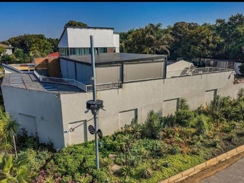 An elevated view of the property's front exterior, featuring a flat roof design, security infrastructure, and established garden landscaping.