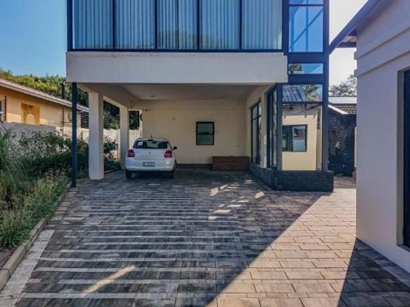 Modern architectural facade featuring a paved driveway, covered parking space, and extensive glass paneling, presenting a contemporary and well-maintained exterior entrance.