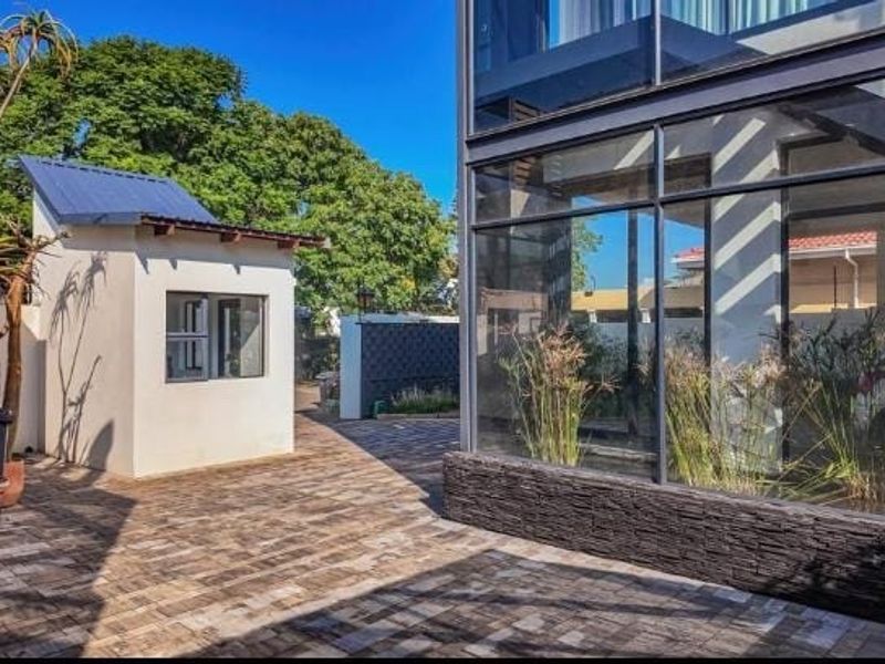 A modern rear courtyard featuring extensive glass walling, stone cladding accents, and a separate outbuilding set against a paved outdoor area.