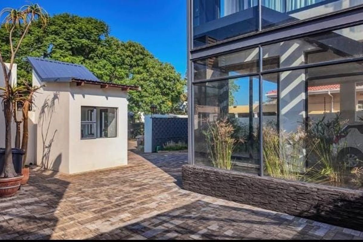 A modern rear courtyard featuring extensive glass walling, stone cladding accents, and a separate outbuilding set against a paved outdoor area.
