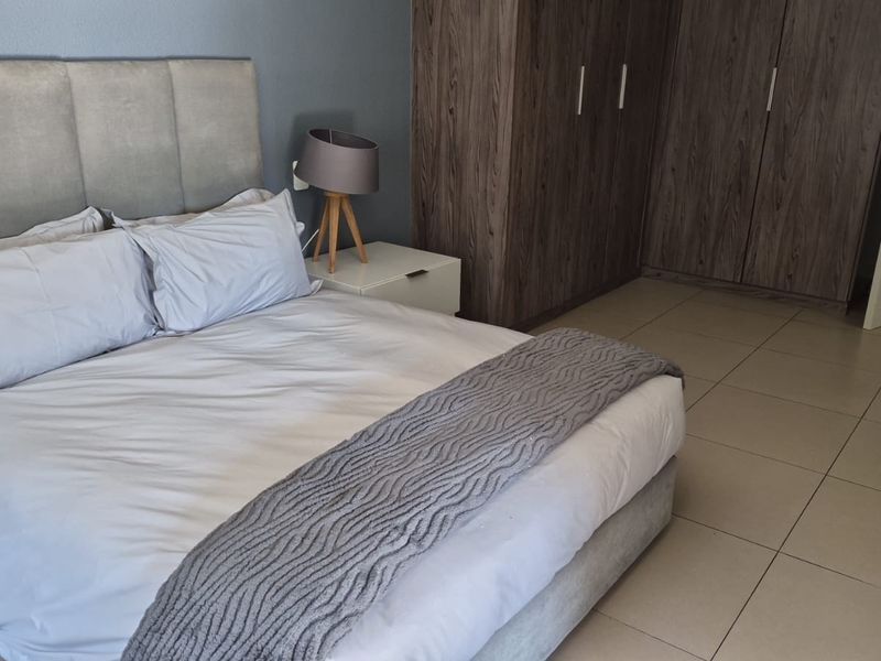 A well-maintained bedroom featuring neutral tiled flooring and modern built-in wooden cupboards, offering a clean and functional living space.