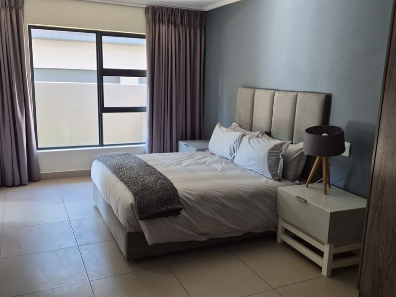 A well-maintained bedroom featuring neutral tiled flooring, large aluminium-framed windows, and a contemporary grey accent wall.
