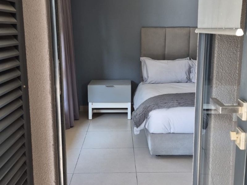 A view into a modern bedroom featuring tiled flooring and recessed lighting, accessed through a sliding door from an outdoor area.