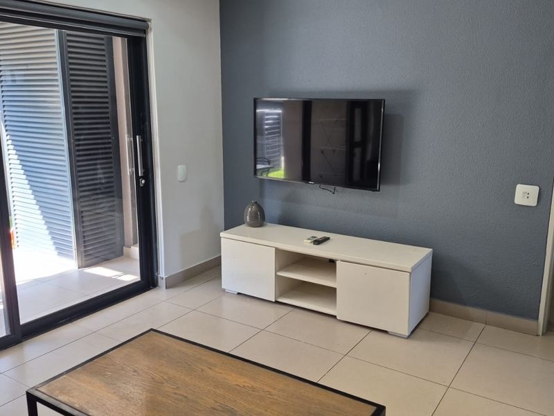A modern living room featuring large sliding glass doors leading to a patio, neutral tiled flooring, and a dark grey accent wall.