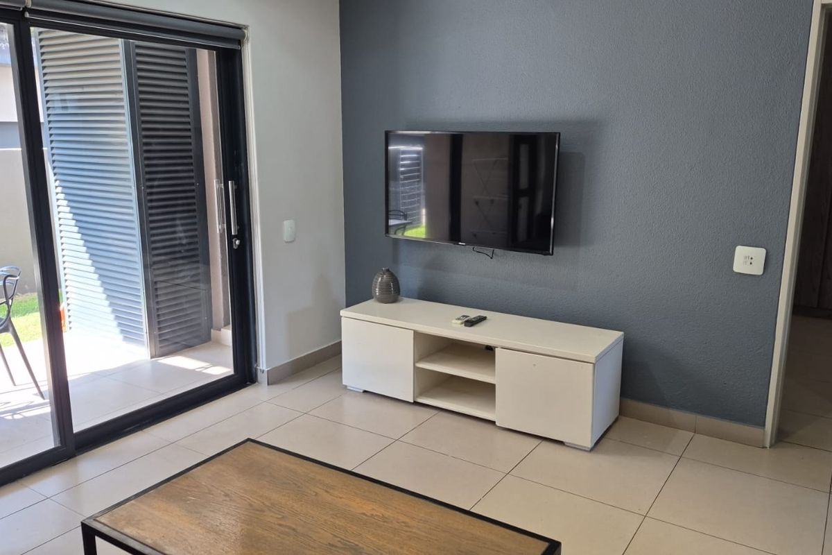 A modern living room featuring large sliding glass doors leading to a patio, neutral tiled flooring, and a dark grey accent wall.