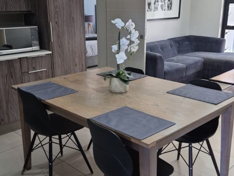 An open-plan living and dining area featuring modern wood-grain cabinetry, neutral tiled flooring, and recessed lighting, creating a cohesive and functional space.
