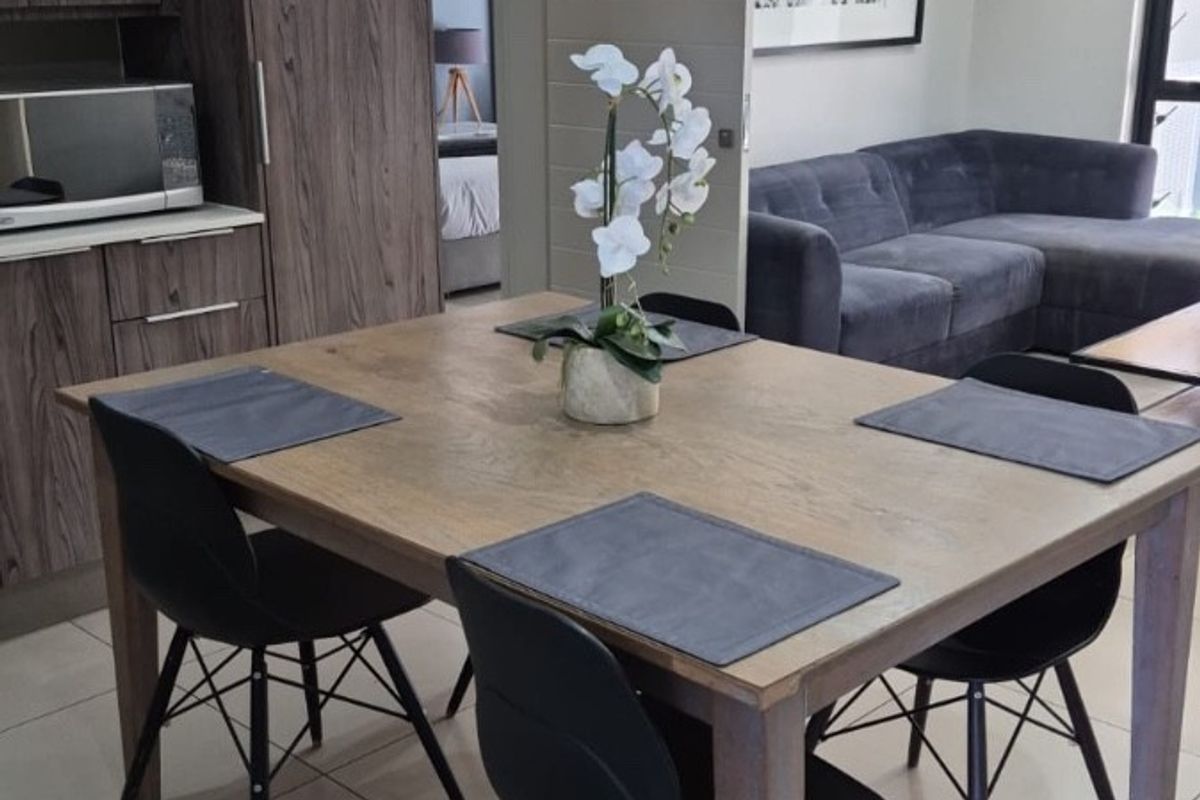 An open-plan living and dining area featuring modern wood-grain cabinetry, neutral tiled flooring, and recessed lighting, creating a cohesive and functional space.