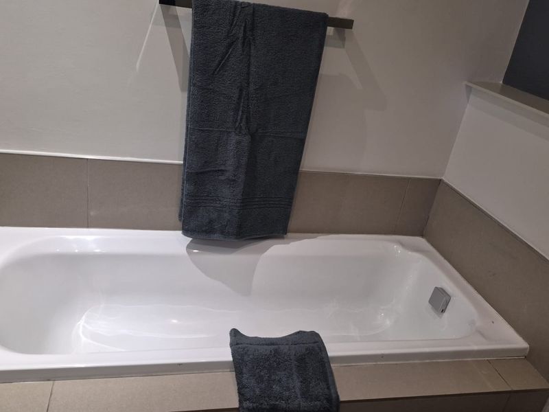 A clean bathroom featuring a built-in bathtub with neutral-toned wall tiling and a modern towel rail.