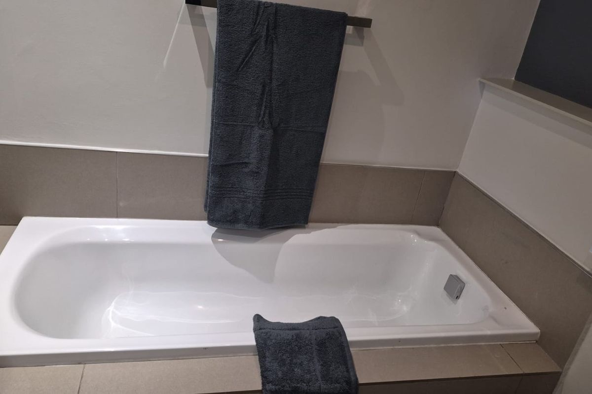 A clean bathroom featuring a built-in bathtub with neutral-toned wall tiling and a modern towel rail.