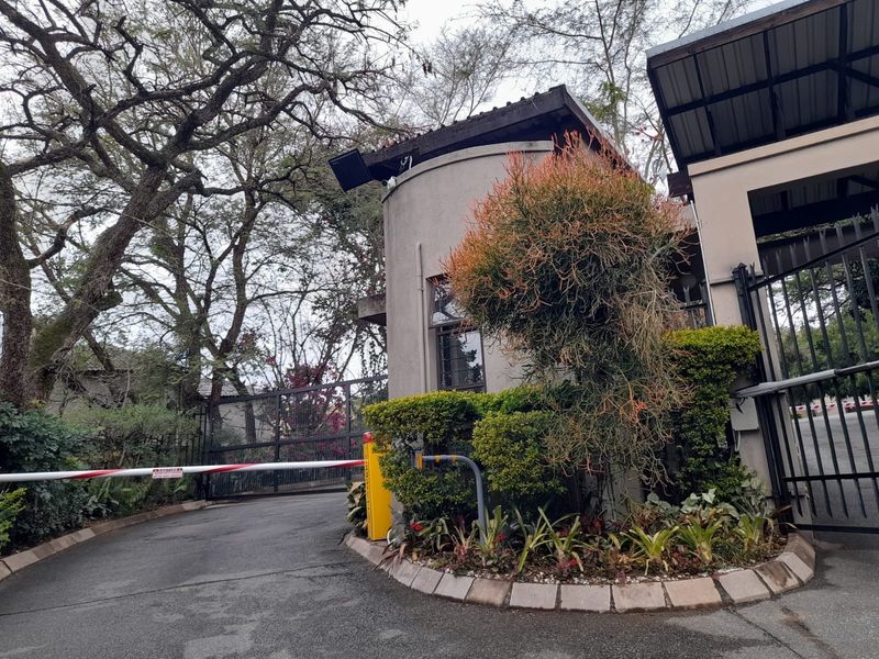 A secure gated entrance to the apartment complex featuring a guard house, boom gate, and established perimeter landscaping.