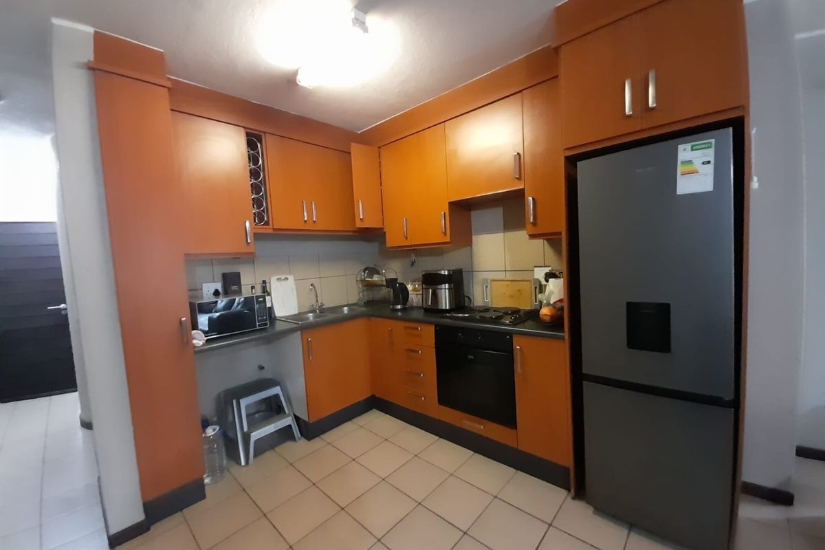 A functional kitchen featuring orange cabinetry, tiled flooring, a built-in oven, and a hob with a tiled backsplash.