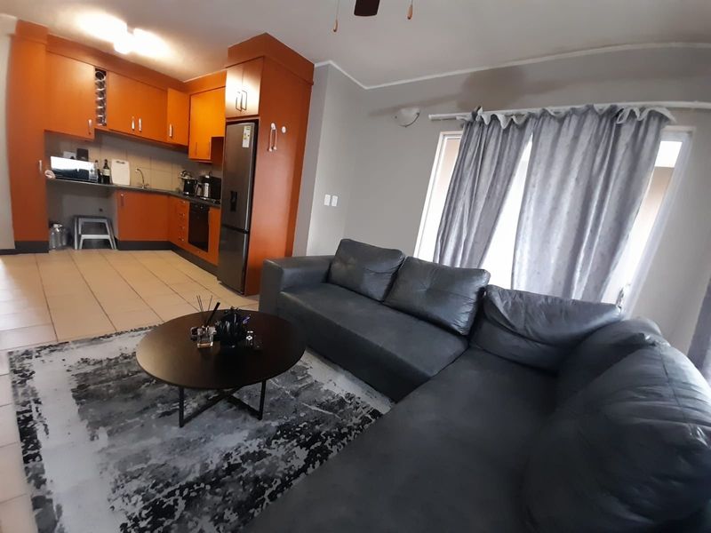 Open-plan living area featuring a kitchen with built-in cabinetry and integrated oven, flowing into a comfortable lounge space with tiled flooring.