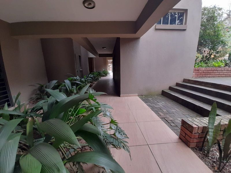 A covered outdoor walkway featuring tiled flooring, concrete steps, and brick retaining walls, leading towards a rear garden area.