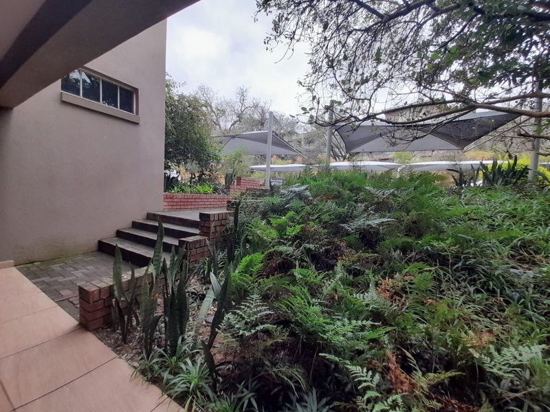 A landscaped garden area featuring brick steps, paved pathways, and overhead shade sails providing cover for the outdoor space.
