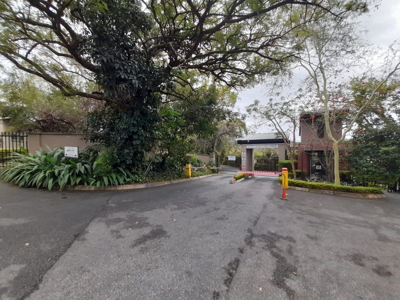 The entrance to the apartment complex features a secure boom gate, guard house, and well-maintained landscaped surroundings.
