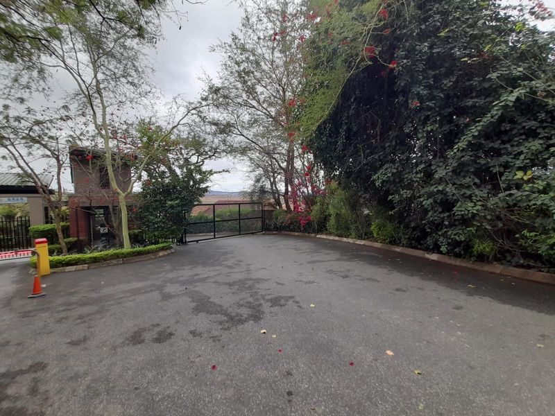 Entrance area of the apartment complex featuring a secure gated access point, asphalt driveway, and established perimeter landscaping.