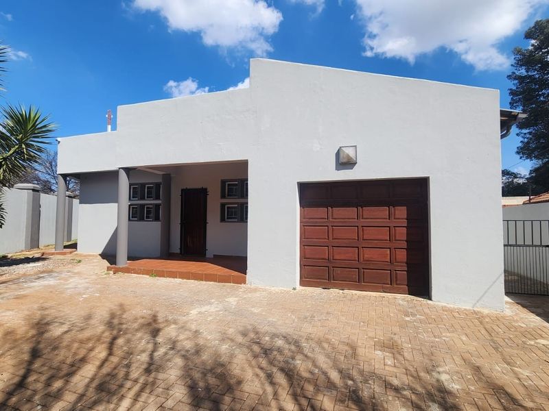 Front view of the property featuring a paved driveway, single wooden garage door, and a covered entrance area with boundary walling.