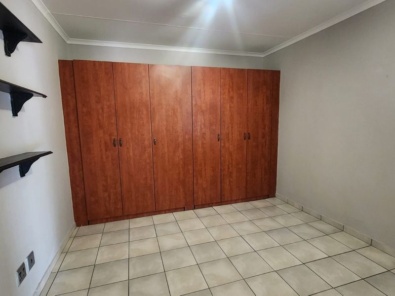 A clean, empty bedroom featuring tiled flooring, neutral walls, and extensive built-in wooden cupboards for storage.