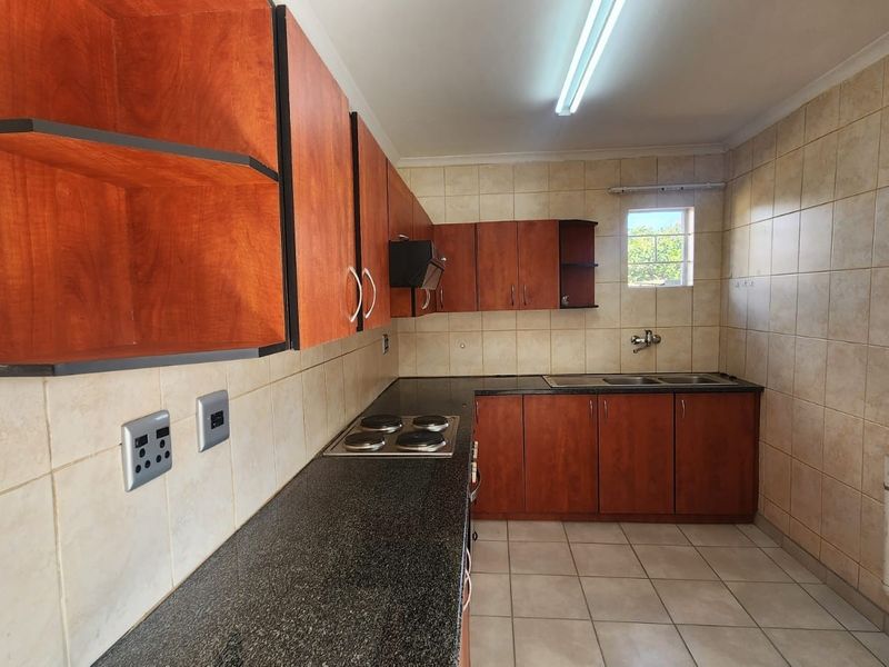 A functional kitchen featuring wood-finish cabinetry, granite countertops, an integrated electric hob, and tiled finishes throughout.