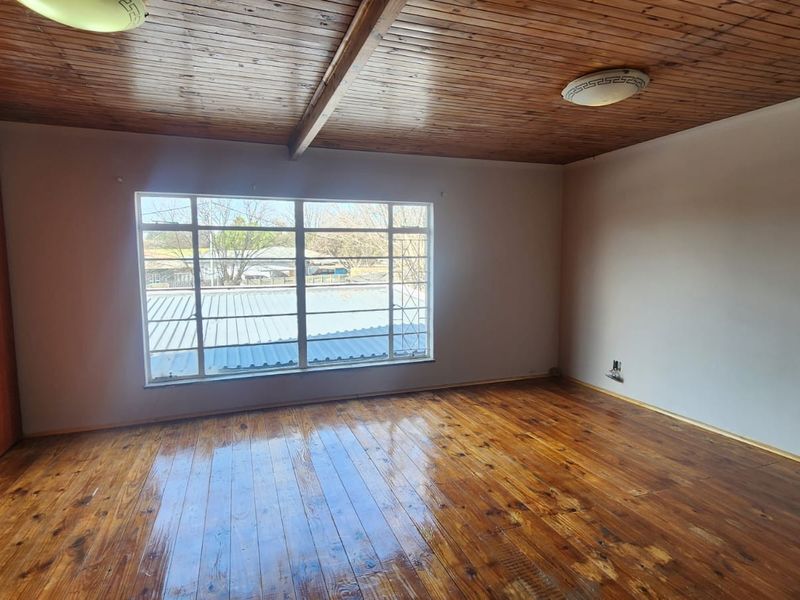A spacious bedroom featuring polished wooden flooring, a timber-clad ceiling, and built-in cupboards, offering a blank canvas for personalization.