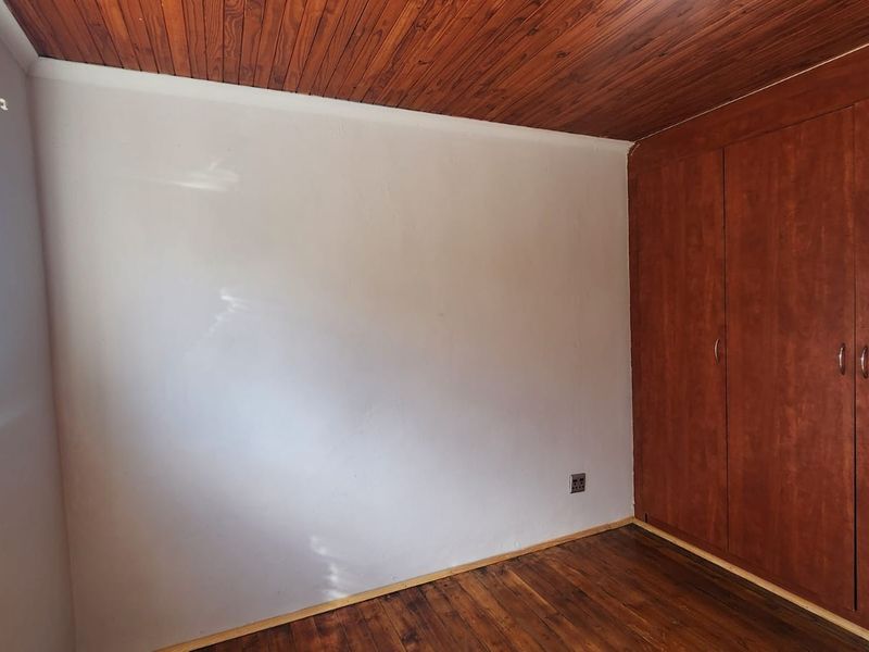 A vacant bedroom featuring built-in wooden cupboards, a timber-paneled ceiling, and original wooden flooring, offering a blank canvas for renovation.