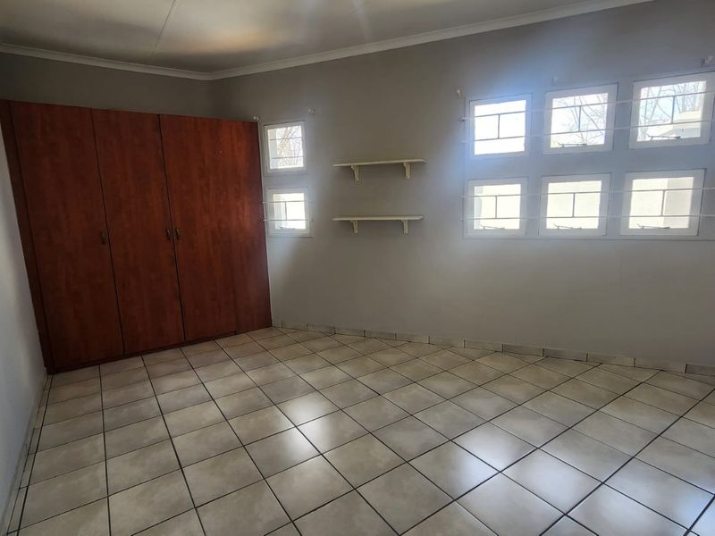A spacious, empty bedroom featuring neutral wall paint, ceramic tiled flooring, and a large built-in wooden wardrobe with ample storage space.