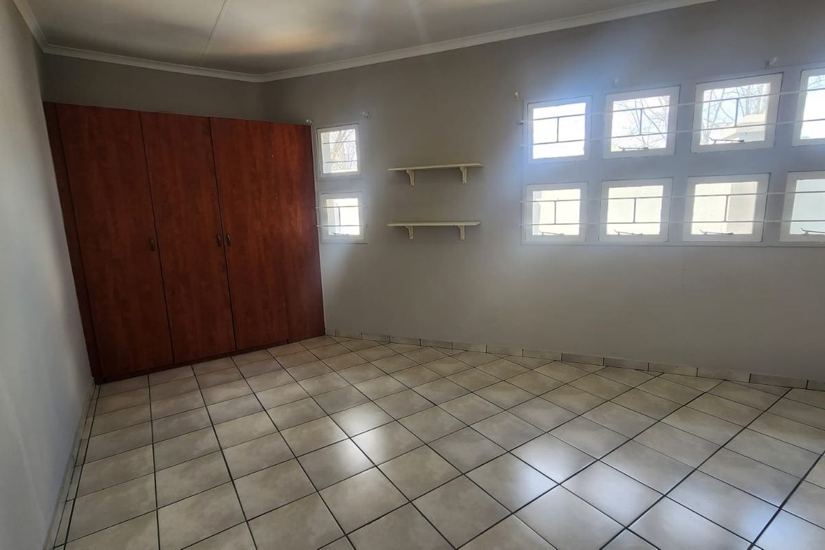 A spacious, empty bedroom featuring neutral wall paint, ceramic tiled flooring, and a large built-in wooden wardrobe with ample storage space.
