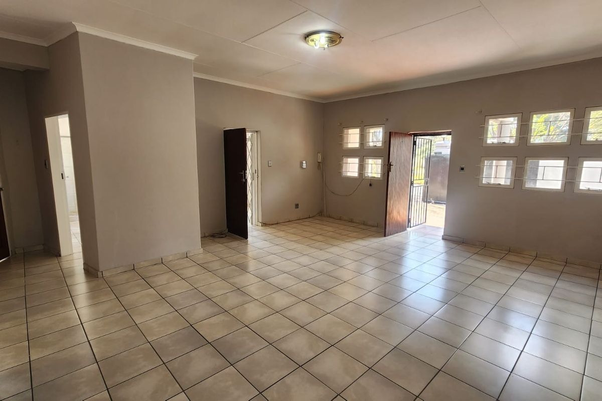 An empty, open-plan living area featuring ceramic floor tiles, multiple windows, and direct access to the exterior via a security gate.