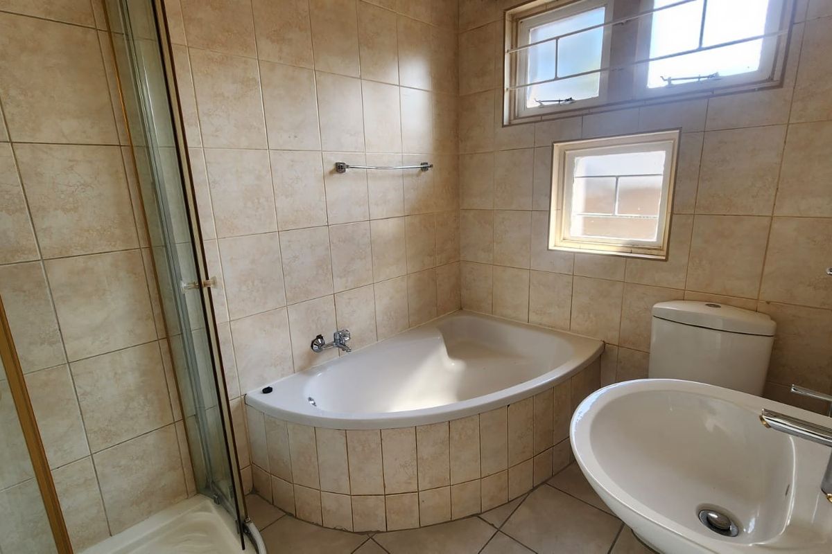 A functional bathroom featuring a corner bathtub, separate shower enclosure, pedestal basin, and toilet with neutral wall and floor tiling.