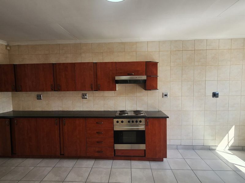 A functional kitchen featuring wooden cabinetry, a built-in oven and hob, extractor fan, and neutral tiled walls and flooring.