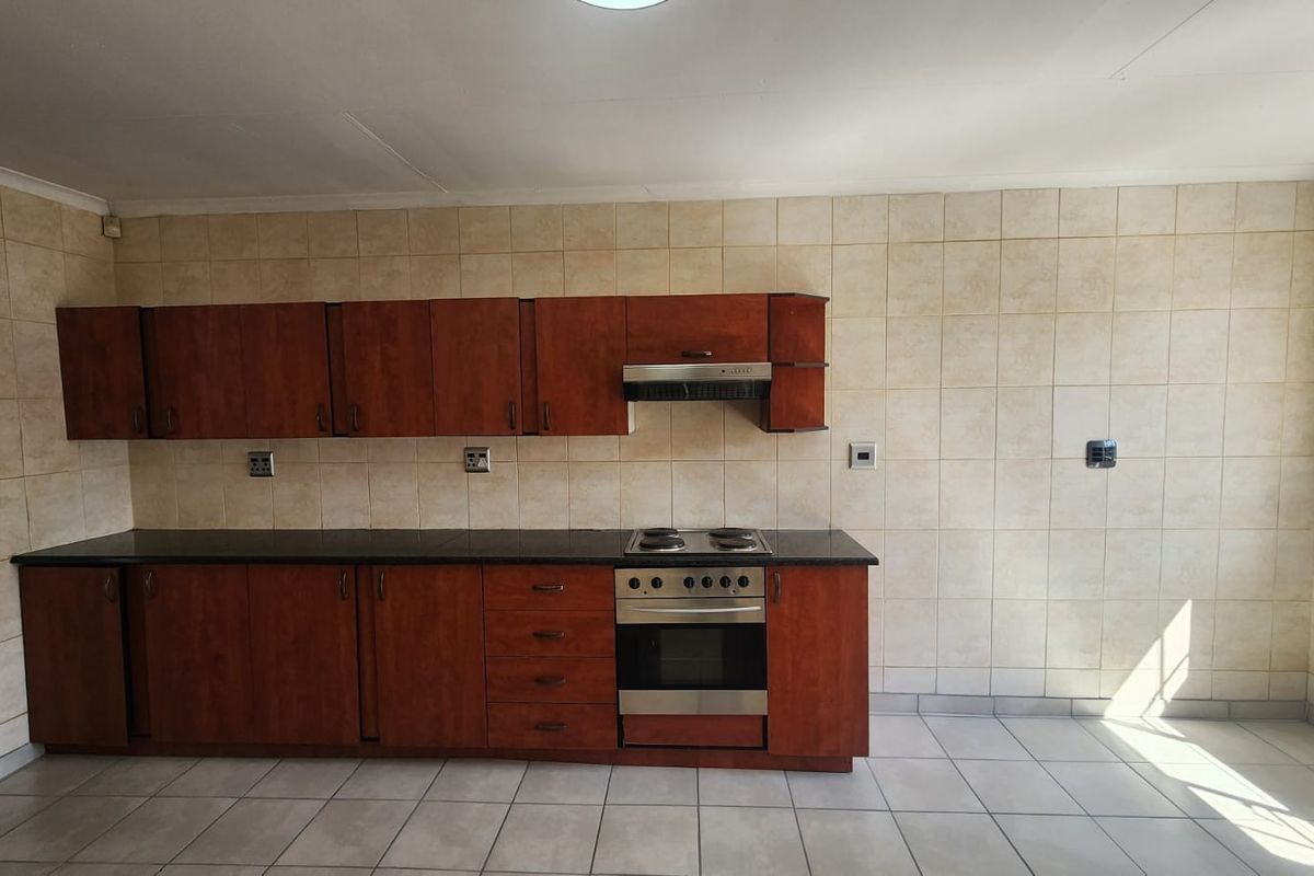 A functional kitchen featuring wooden cabinetry, a built-in oven and hob, extractor fan, and neutral tiled walls and flooring.
