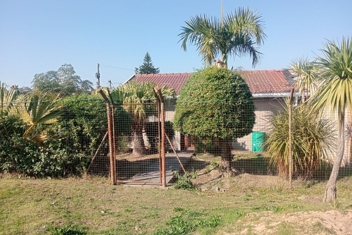 Rear exterior view of the property featuring a tiled roof, concrete pathway, and wire mesh perimeter fencing with a metal gate.