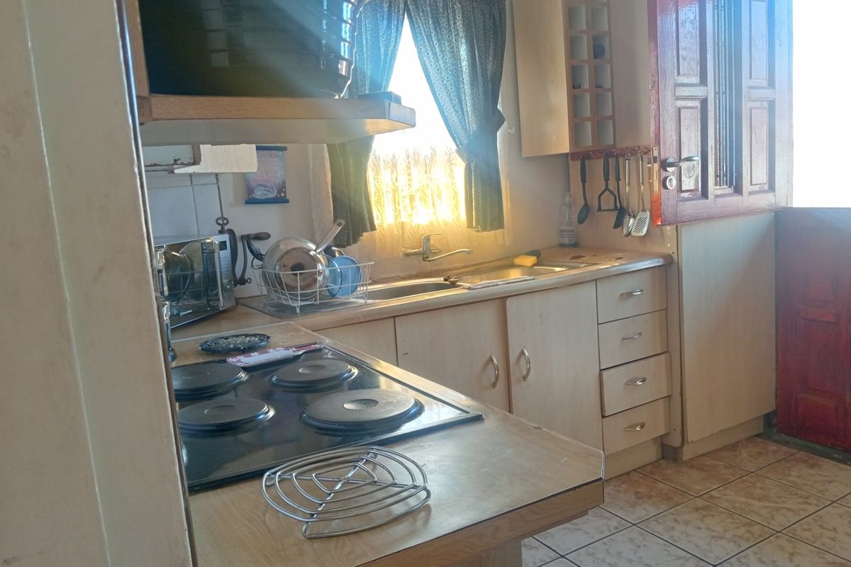 A functional kitchen featuring built-in cabinetry, laminate countertops, an electric hob, and tiled flooring, offering potential for a modern cosmetic update.