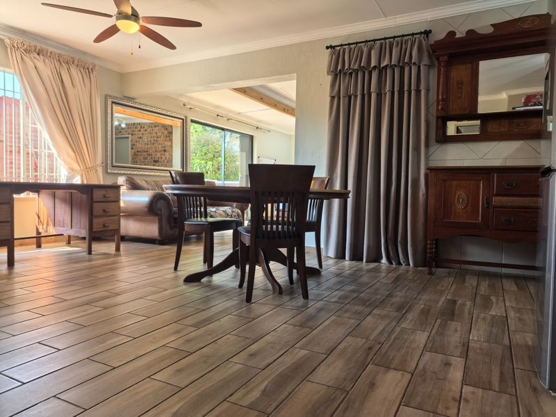 Spacious open-plan living and dining area featuring wood-look tile flooring, exposed ceiling beams, and a ceiling fan, with access to an outdoor space.