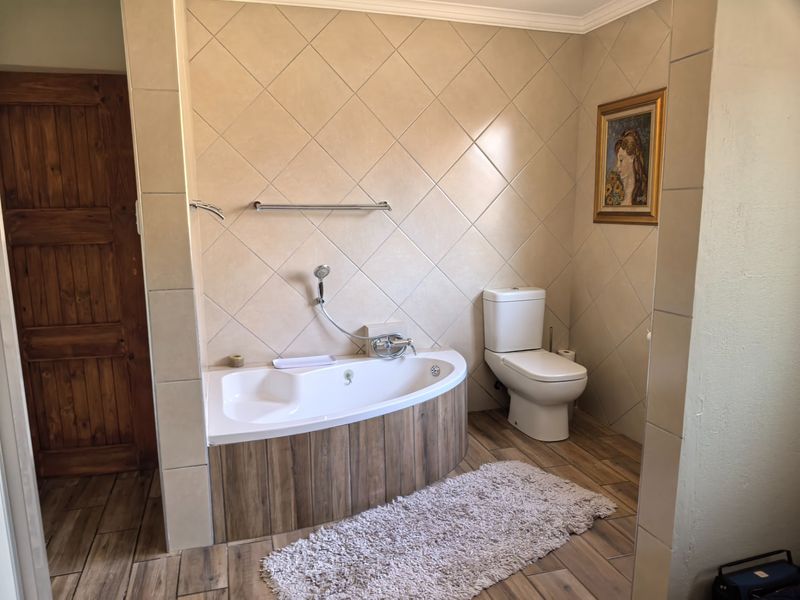 A well-maintained bathroom featuring a corner bathtub with a handheld shower attachment, a standard toilet, and neutral-toned wall and floor tiling.