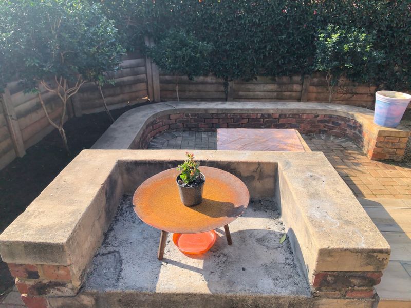 Rear garden area featuring a built-in brick braai, curved masonry seating wall, and paved patio space enclosed by timber fencing and established hedging.