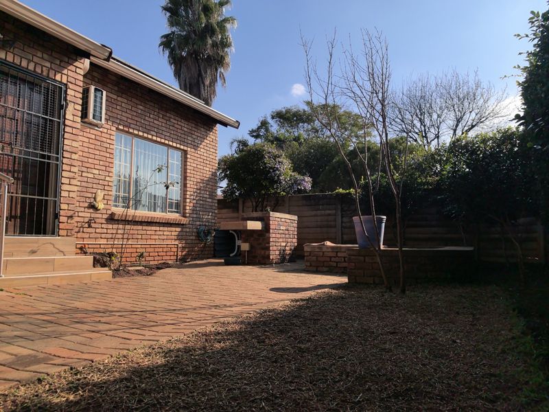 A rear exterior view of a townhouse featuring a brick facade, paved patio area, and a built-in brick braai structure within a private garden.